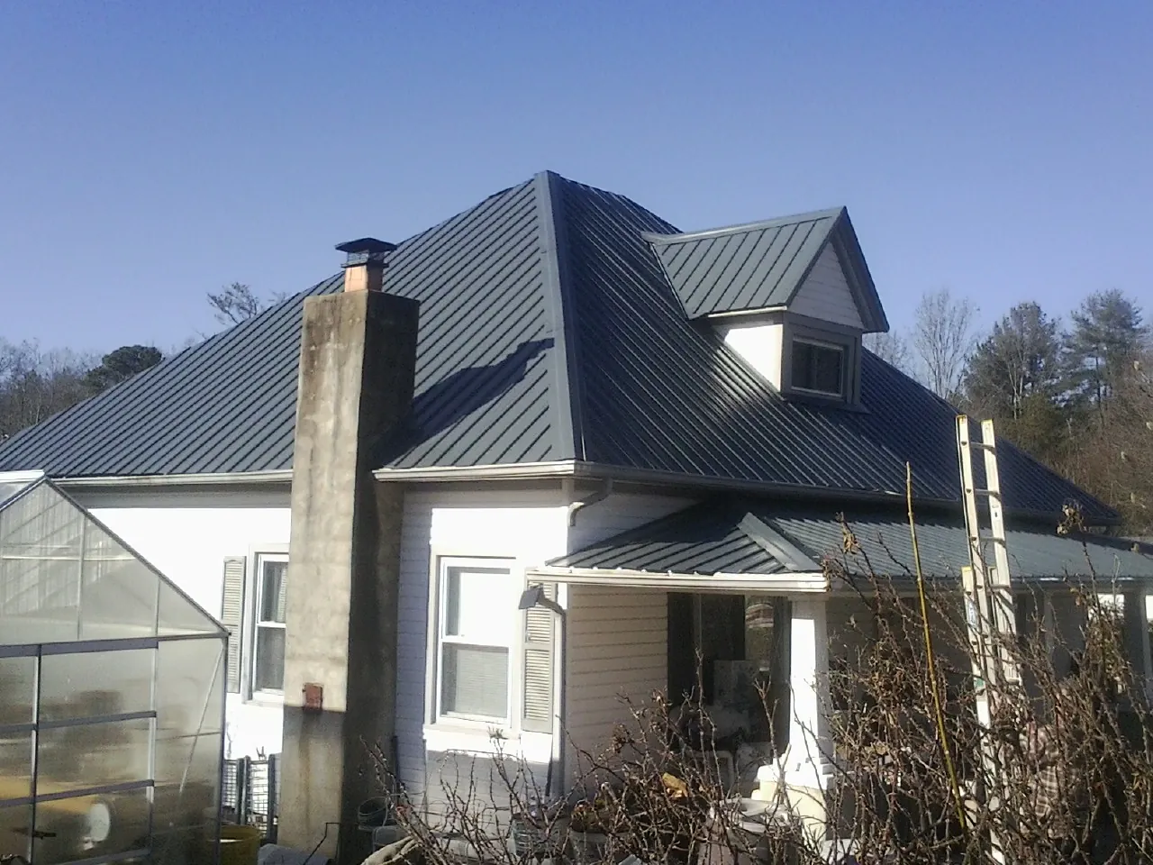 Dark blue standing seam metal roof on a white farmhouse with dormer — Slate & Tile Roof Repair by Roofing Brothers in Musselshell