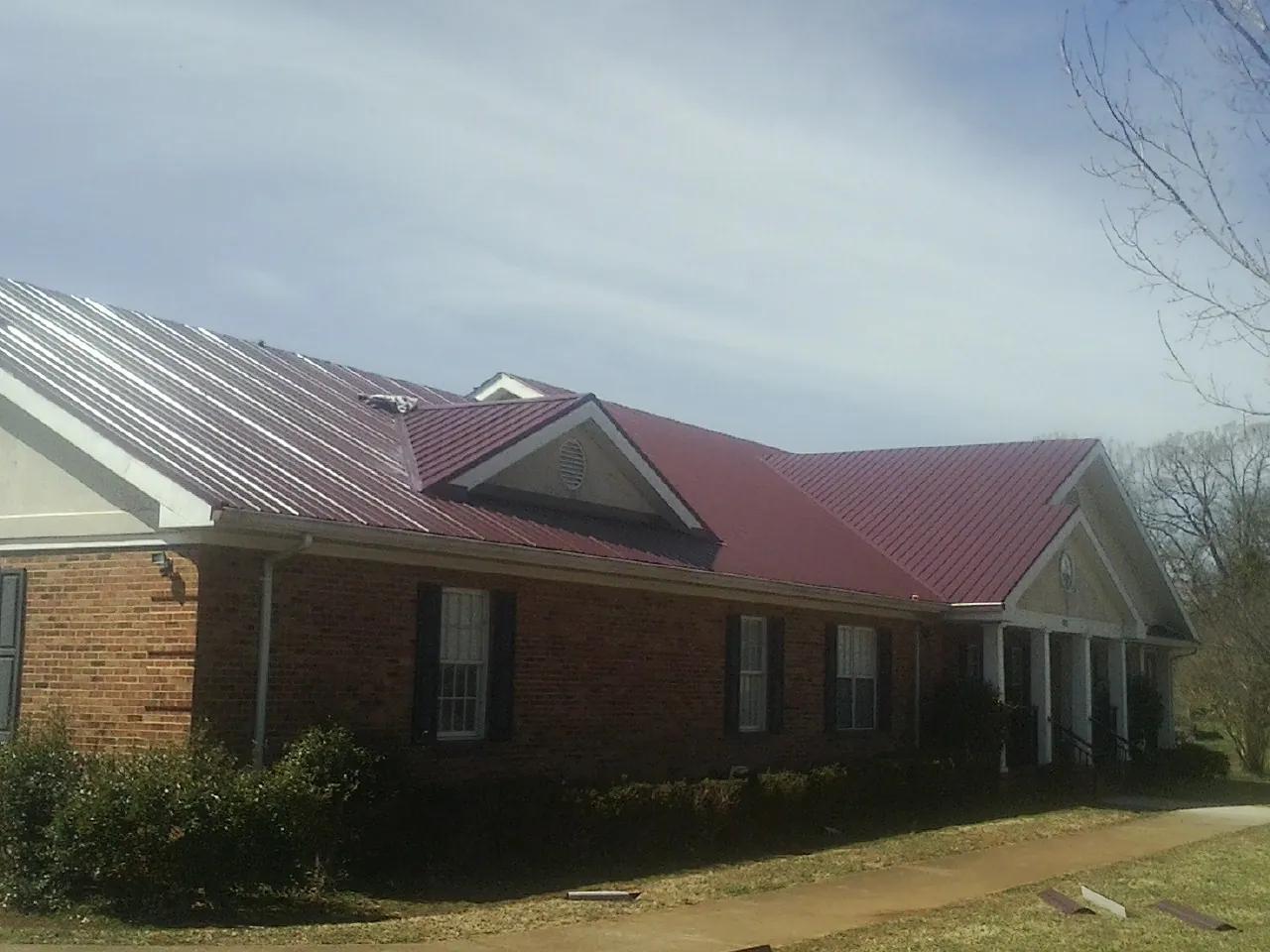 Red metal roof with gabled entries on a long brick building, from a Hail Damage Roof Repair job in Musselshell